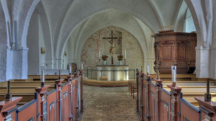 Interiør af en kirke med høje buegange og træbænke.