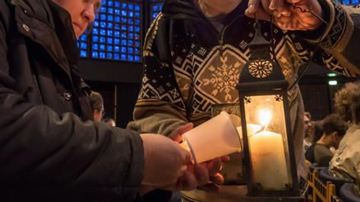 Menschen, die in einer Kirche mit bunten Glasfenstern eine Kerze anzünden.