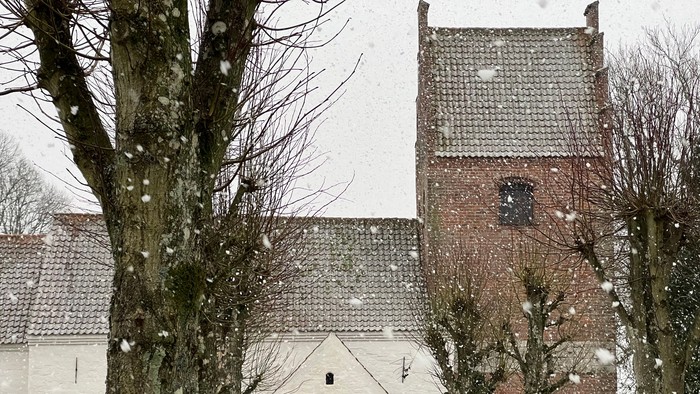 En snødekkede kirke med tårn og træer.