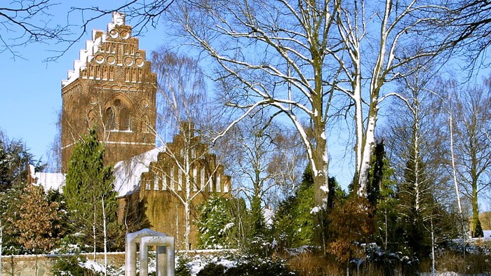 En snedækket park med en højtårnet kirke i baggrunden
