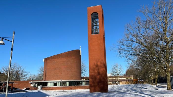 En rød murstenskirke med klokketårn og snedækket jorden foran