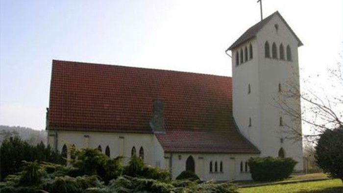 Eine malerische weiße Kirche mit rotem Ziegeldach und hohem Glockenturm in einer gepflegten Grünanlage.
