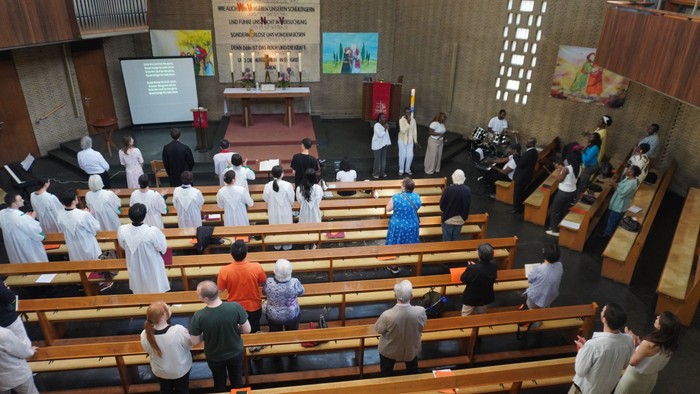 Blick von oben auf einen Kirchenraum, viele Menschen, einige tragen weiße Chorkleidung.