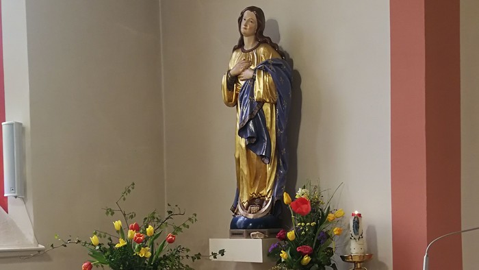 In der Kirche steht eine Statue der Jungfrau Maria mit Blumen und Kerzen.