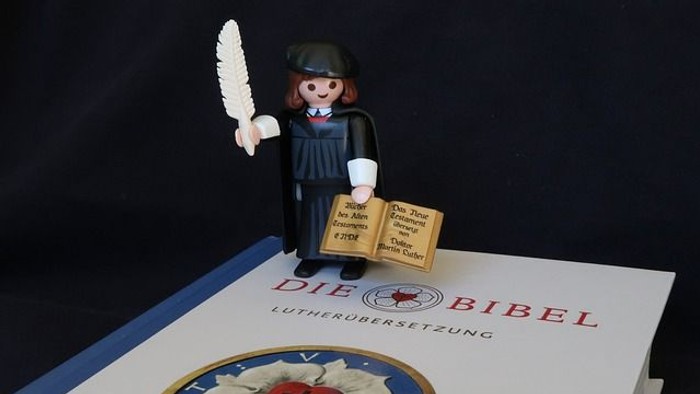 Martin Luther als Spielfigur steht auf einer Bibelausgabe mit Lutherübersetzung.