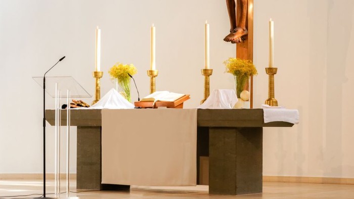 Moderner Kirchenaltar mit einem hölzernen Kruzifix, Kerzen, Blumen und einem Lesepult mit religiösen Büchern.