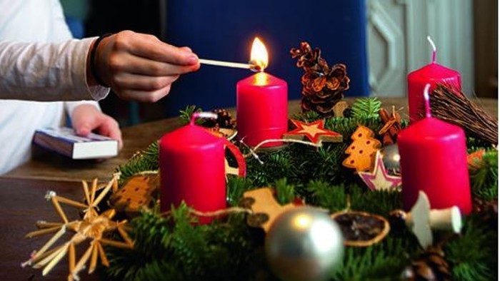 Person zündet rote Kerzen auf einem Adventskranz an.