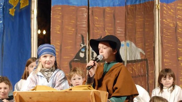 Kinder führen ein Theaterstück in mittelalterlichen Kostümen auf, wobei ein Kind in ein Megafon spricht.