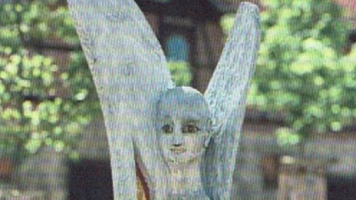 Eine hölzerne Statue eines Engels namens Michael steht friedlich in einem Garten im Freien.