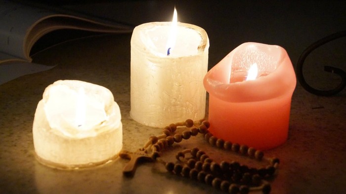 Drei brennende Kerzen und ein Rosenkranz auf einem Tisch.