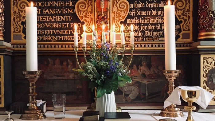 Indre del af kirke med blomster og lysstaker på alteret