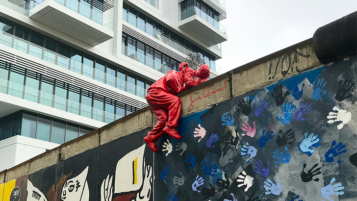 Eine Person in einem roten Kostüm klettert eine mit Graffiti, Handabdrücken und urbaner Kunst bedeckte Wand hinauf.