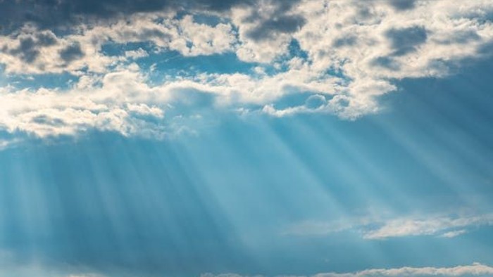 Sonnenlicht bricht durch verstreute Wolken am blauen Himmel.