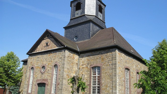 Außenansicht der evangelischen Kirche in Veckerhagen. Natursteingebäude mit hohen Rundbogenfenstern.