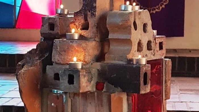 Auf einem Tisch stehen Kerzen in einer Steinskulptur vor einem farbenfrohen Hintergrund