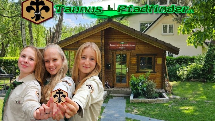 Drei Pfadfinder in Uniformen posieren gemeinsam vor einer Holzhütte mit der Aufschrift „Taunus Pfadfinder“.
