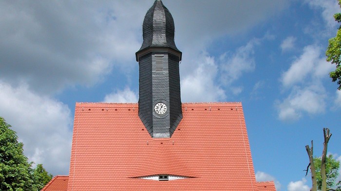 Kleine weiße Kirche mit rotem Dach und schwarzem Turm.