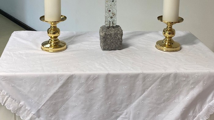 To alteret er dekket med et hvidt tøj med blomster, og der er to lysstake med lysede lygter på hver side af et sten kors.