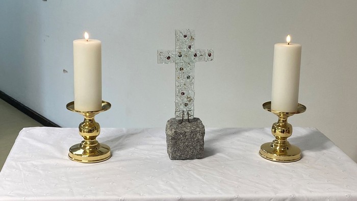 To alteret er dekket med et hvidt tøj med blomster, og der er to lysstake med lysede lygter på hver side af et sten kors.