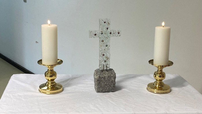To alteret er dekket med et hvidt tøj med blomster, og der er to lysstake med lysede lygter på hver side af et sten kors.