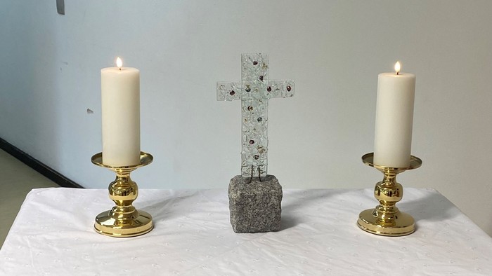 To alteret er dekket med et hvidt tøj med blomster, og der er to lysstake med lysede lygter på hver side af et sten kors.