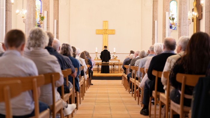 En menighed sidder i en kirkeskibs midtergang under en højtidelig gudstjeneste og vender sig mod et centralt alter med et kors.
