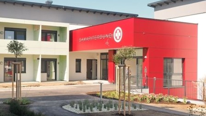 Das Bild zeigt ein modernes Gebäude mit einem roten und weißen Farbschema und einem gut gepflegten Außenbereich.