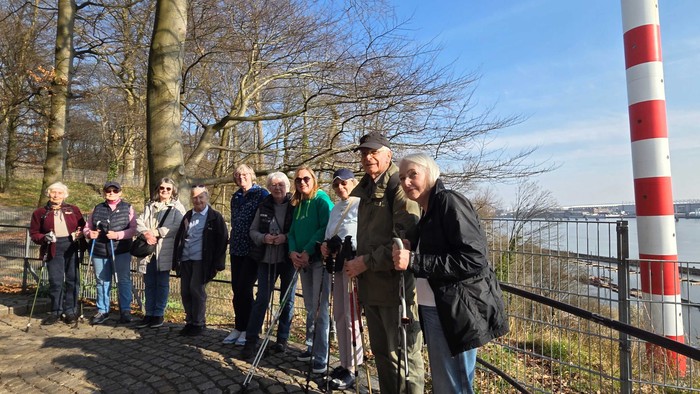Gruppe von Menschen, die im Freien in der Nähe einer rot-weißen gestreiften Leuchtturm-ähnlichen Struktur an einem malerischen Wasserufer posieren.