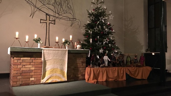 In der Kirche steht ein geschmückter Weihnachtsbaum neben einem Kamin mit Kerzen.