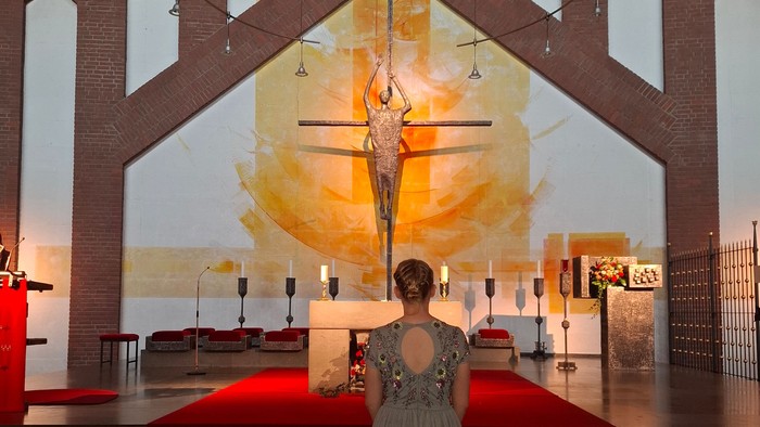 Eine Frau steht elegant unter einem beeindruckenden Glasfenster-Kruzifix im Inneren einer modernen Kirche.