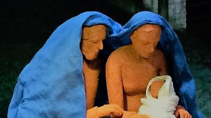 Drei Figuren in blauen Umhängen, eine hält ein Baby im weißen Tuch.
