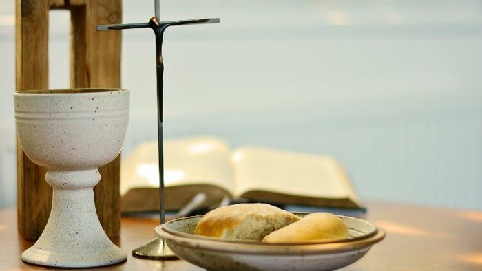 Heilige Kommunionsgegenstände, darunter Kelch, Brot und eine offene Bibel auf einem Holztisch.