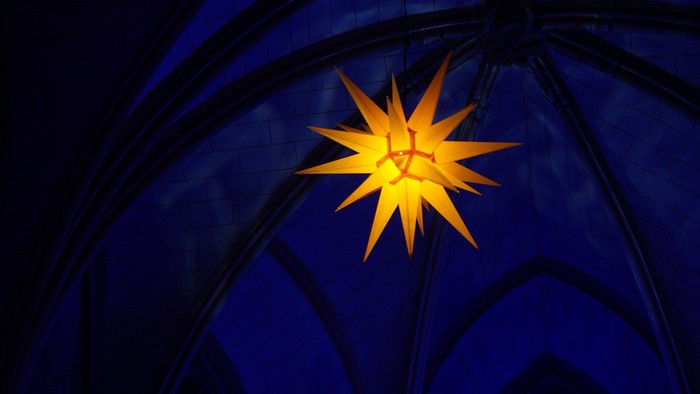 Leuchtender Herrnhuter Stern in dunklem Kirchengewölbe
