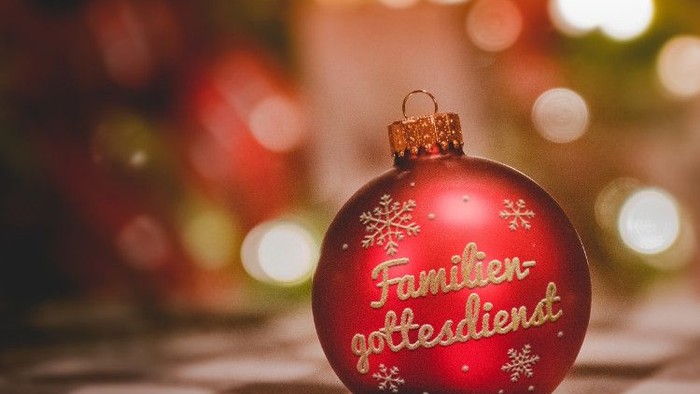 Ein roter Weihnachtschmuck mit deutschem Text liegt auf einer strukturierten Oberfläche.