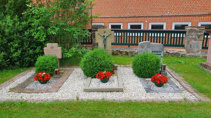 Gepflegter Gräberbereich mit roten Blumen und Büschen vor Backsteingebäude