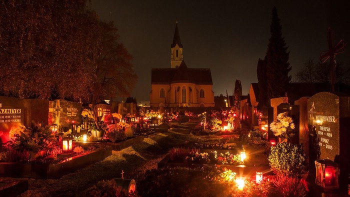 Nachtsfriedhof mit brennenden Kerzen und Kirche im Hintergrund