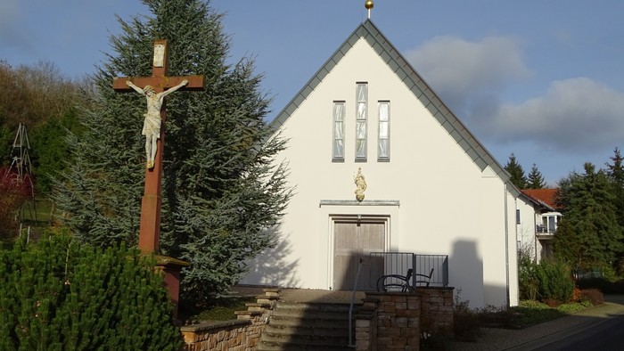 Kleine weiße Kirche mit Kreuz und Kreuzigungsgruppe davor