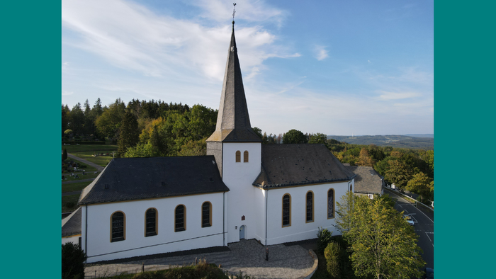 Weiße Kirche mit hohem Turm in ländlicher Umgebung