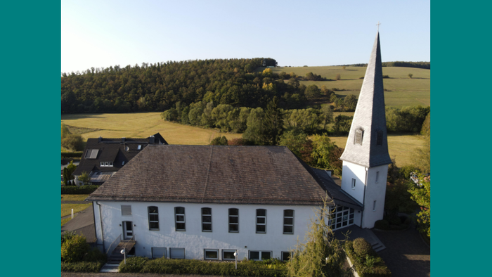 Weißes Gebäude mit spitzem Turm in ländlicher Umgebung