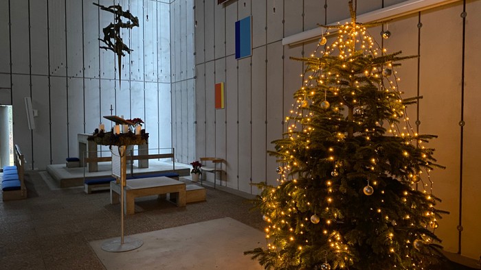 Et tændt juletræ i et mørkt og rummeligt kirkelokale