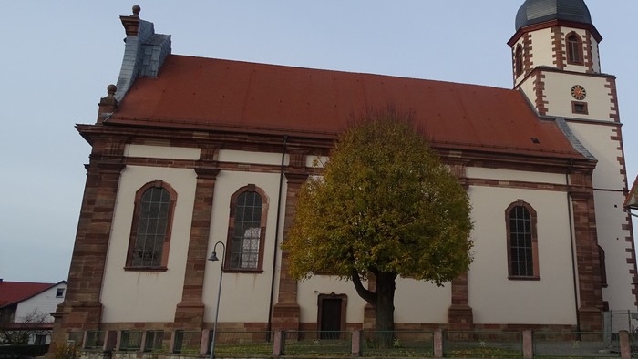Kirchengebäude mit rotem Dach und hohem Turm neben Baum