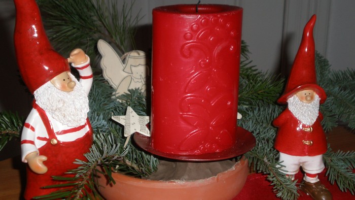 Drei Weihnachtsgnome flankieren eine rote Kerze mit Tannenzweigen