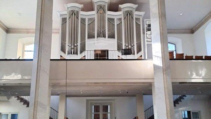 Elegante Kircheninnenausstattung mit einer großen Pfeifenorgel, die auf klassischen Säulen erhöht steht, sowie gestuften Sitzreihen und Kirchenbänken.