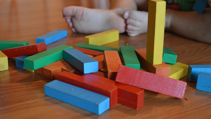 Bunte Holzklötze auf einem Holzboden, Kinderhände im Hintergrund