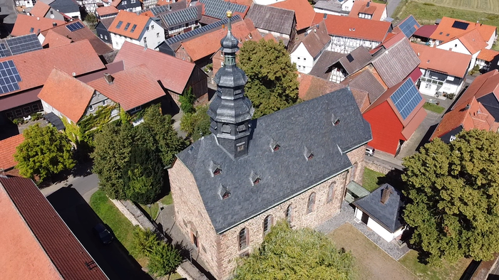 Luftaufnahme eines Kirchgebäudes inmitten eines Dorfes mit roten Dächern.