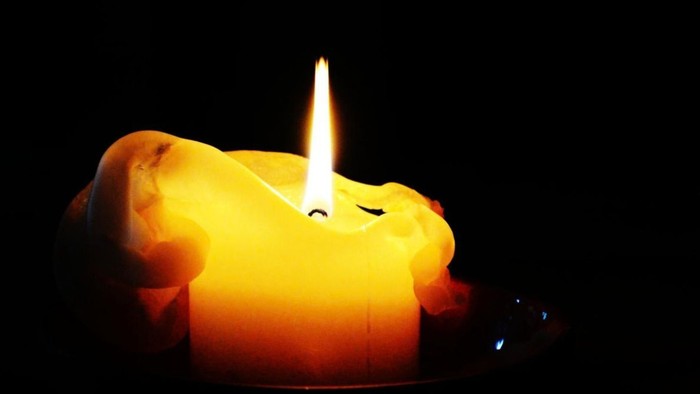 Eine leuchtende Kerzenflamme erhellte sich in einer dunklen, handförmigen Silhouette.