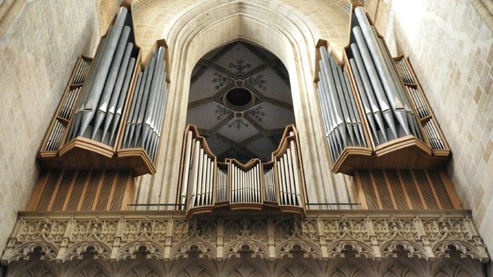 Große Pfeifenorgel in einem prunkvollen, historischen Kircheninnenraum mit aufwendiger Steinmetzarbeit und Bogenfenstern.
