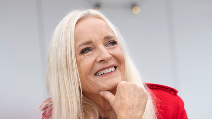 En glad kvinde i en rød jakke poserer eftertænksomt med et varmt smil udendørs.