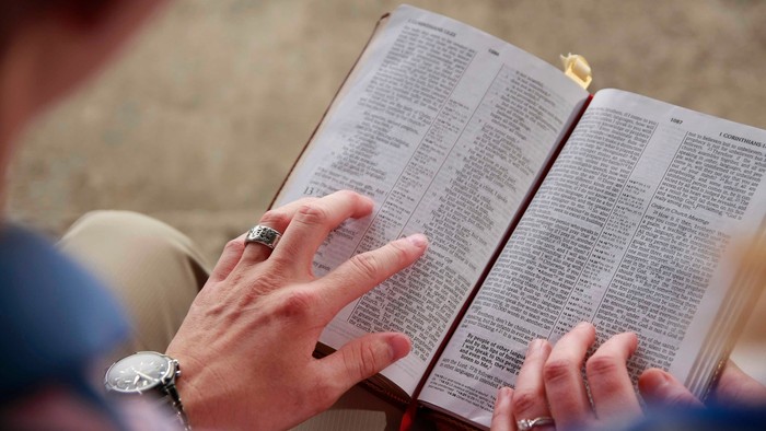Eine Person liest in der Bibel, die auf ihren Knien liegt.