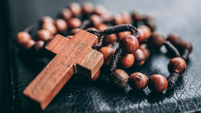Holzrosenkranz mit Kreuz auf einer dunklen, strukturierten Oberfläche.